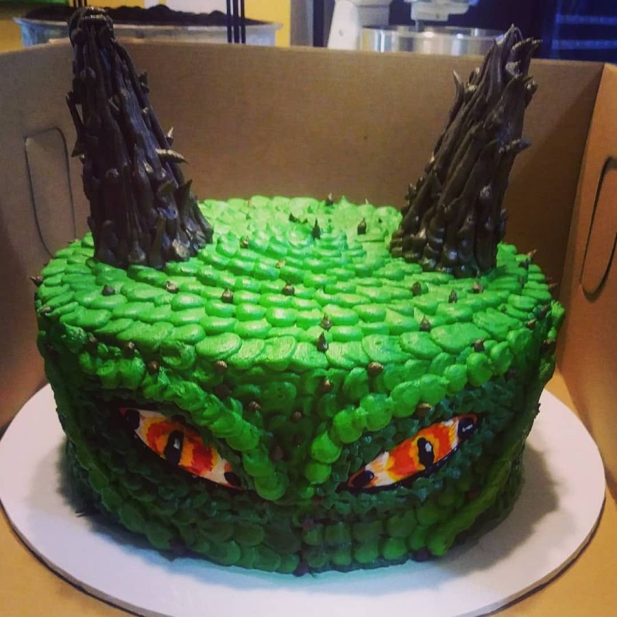 Green buttercream dragon scale cake with horns and fiery eyes