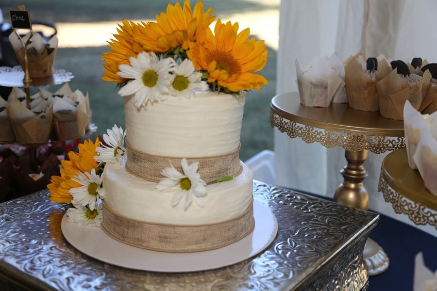 Two-tier white buttercream wedding cake with burlap ribbon, sunflowers and daisies